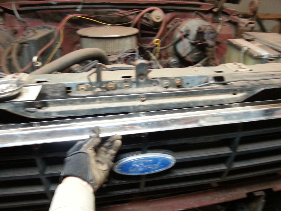 Gloved hand removing the front grille from a Ford truck during a restoration
