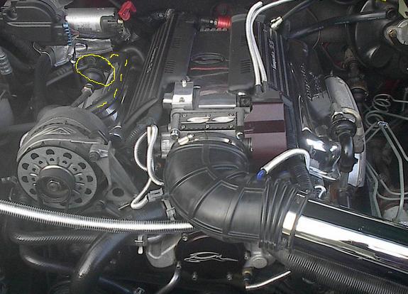 Close-up of a car's engine bay with various hoses, wires, and engine components visible. A chrome air intake tube is prominent