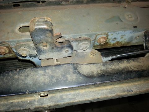 Hood latch mechanism mounted on the front sheet metal of a classic truck