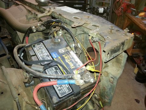 Car battery and battery cables sitting on a workbench with frame and tools