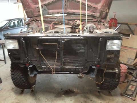 Front of a classic truck with headlights and radiator support, hood up, in a garage