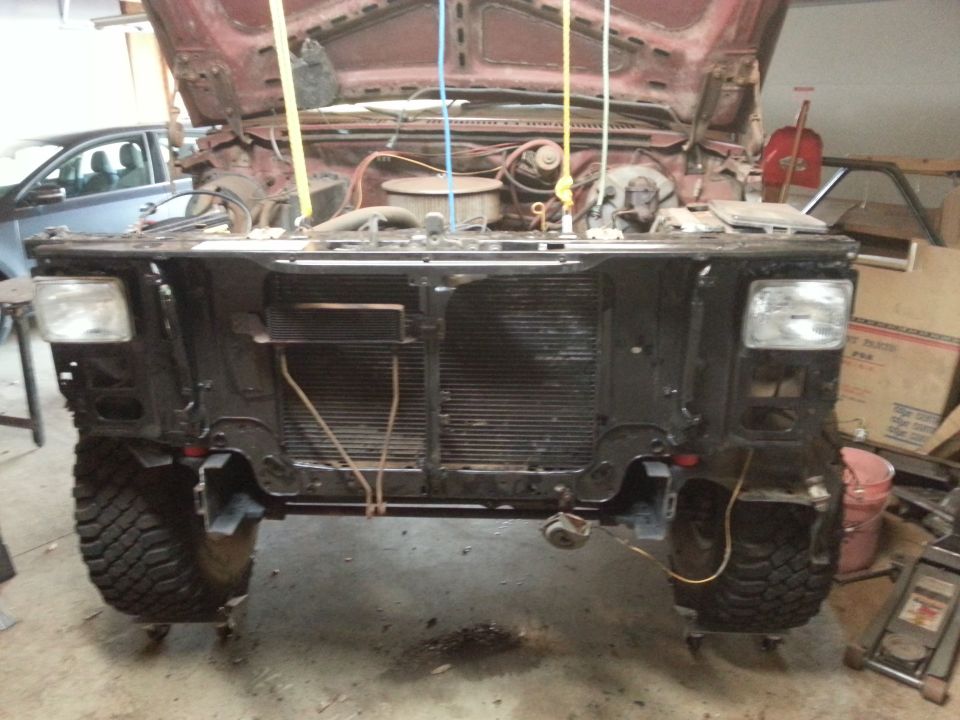 Front of a classic truck with headlights and radiator support, hood up, in a garage