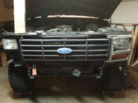 Front of a Ford truck with chrome and black grille and headlights, hood up