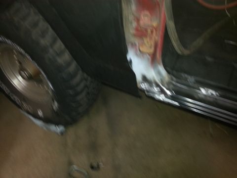 Blurry photo of a vehicle rocker panel and tire during bodywork in a garage
