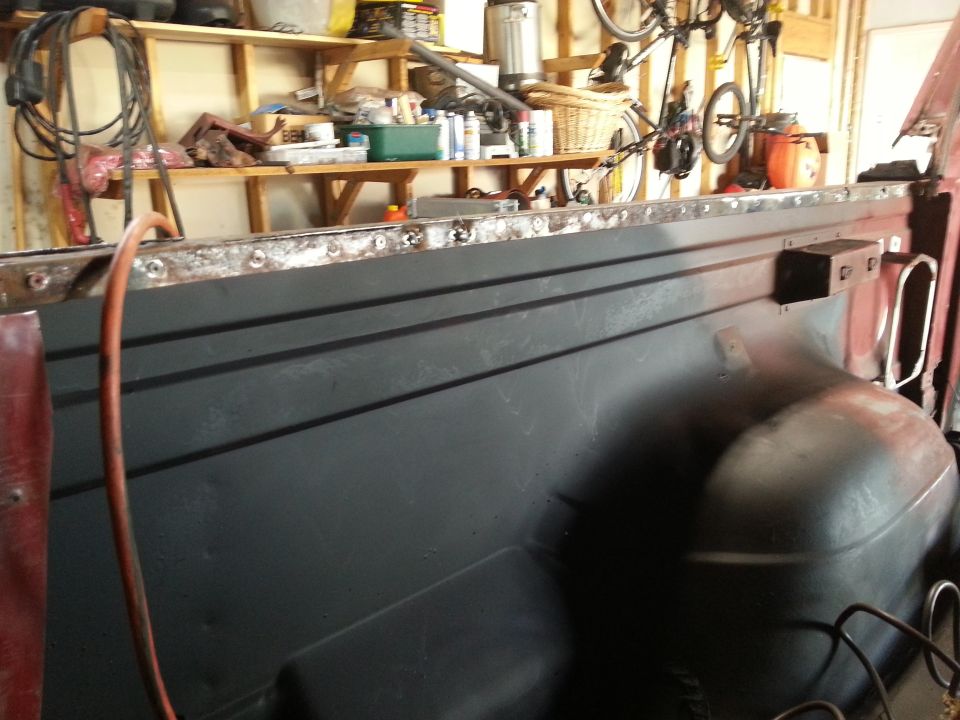 Photo of a primered truck bed side with welded top rail in a garage