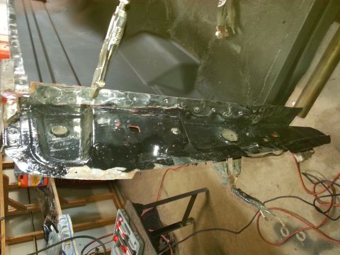 Photo of a black-painted vehicle frame rail or panel resting on a workbench