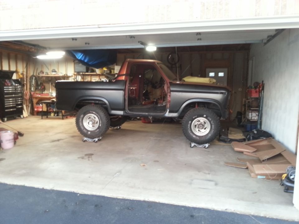 Photo of a primered Ford truck on dollies inside a home garage