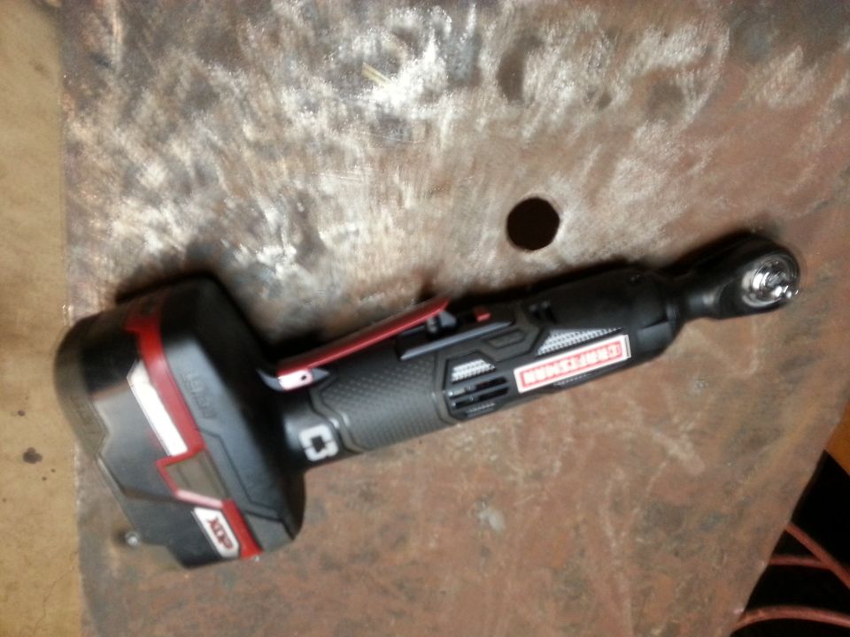 Photo of a cordless ratchet wrench resting on a rusty metal surface
