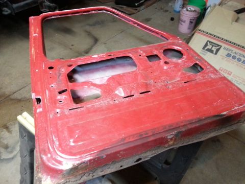 Photo of a stripped red vehicle door shell laid on a workbench
