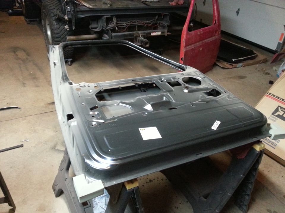 Photo of a bare-metal vehicle door shell on a stand in a garage