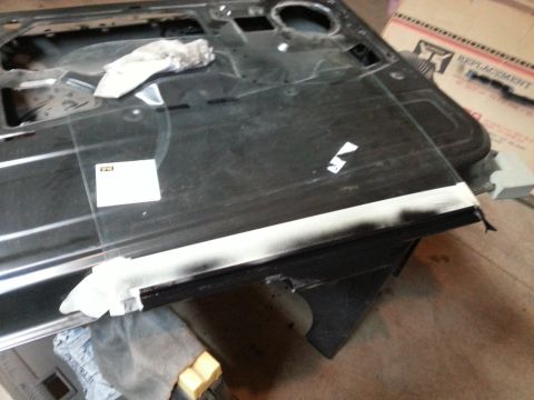 Photo of a black vehicle door interior with glass being fitted in a garage