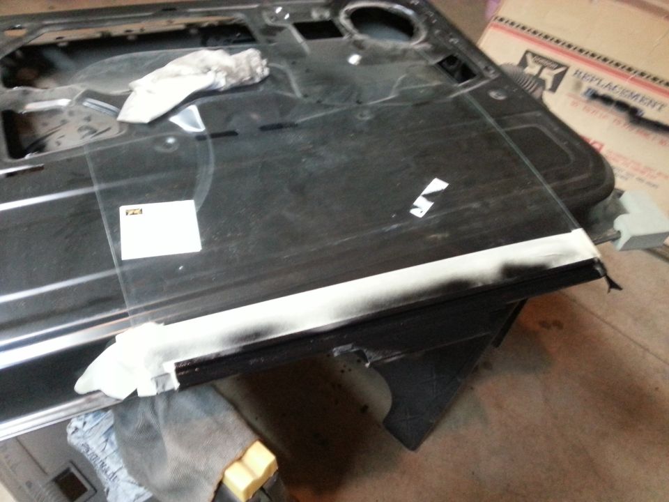 Photo of a black vehicle door interior with glass being fitted in a garage