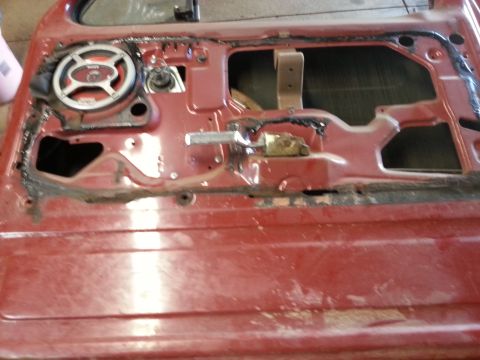 Photo of a red vehicle door interior with speaker and window mechanism