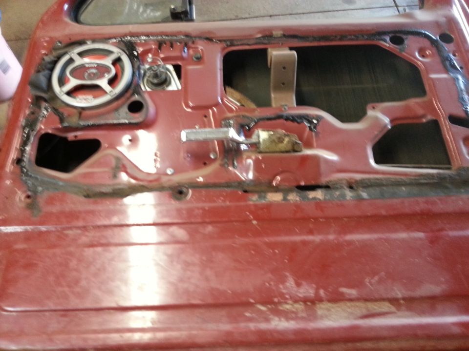 Photo of a red vehicle door interior with speaker and window mechanism