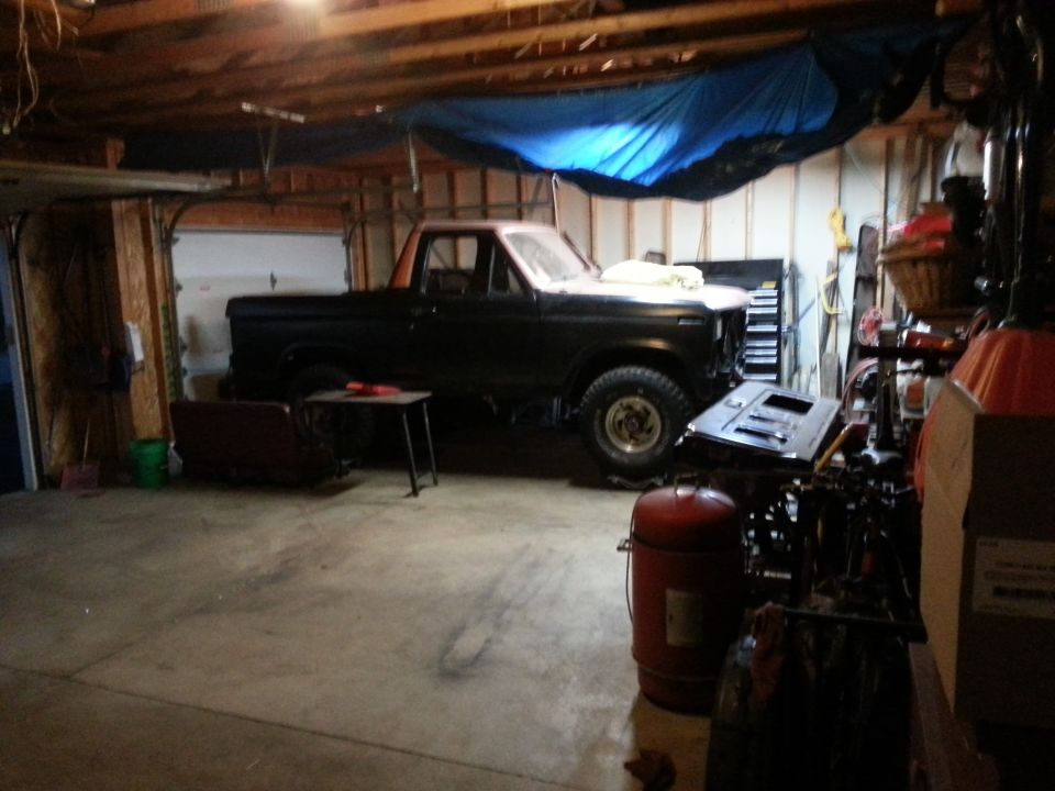 Black classic Ford pickup truck parked inside a wood-framed garage