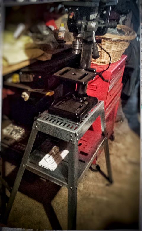 Benchtop drill press mounted on a metal stand in a workshop