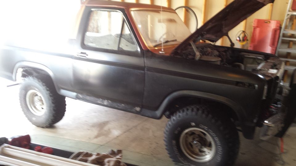 Classic Ford Bronco with hood open inside a garage