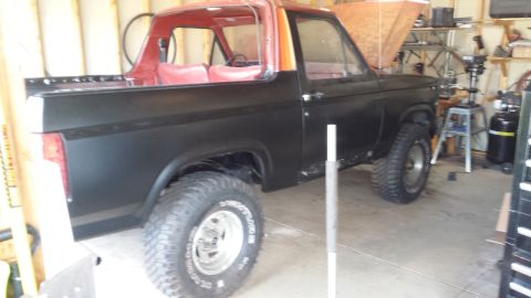 Lifted black and red classic Ford Bronco parked in a garage