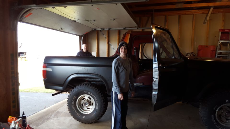 Two people standing with a classic Ford Bronco in an open garage