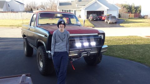 Person standing beside a lifted Ford Bronco with light bar in a driveway
