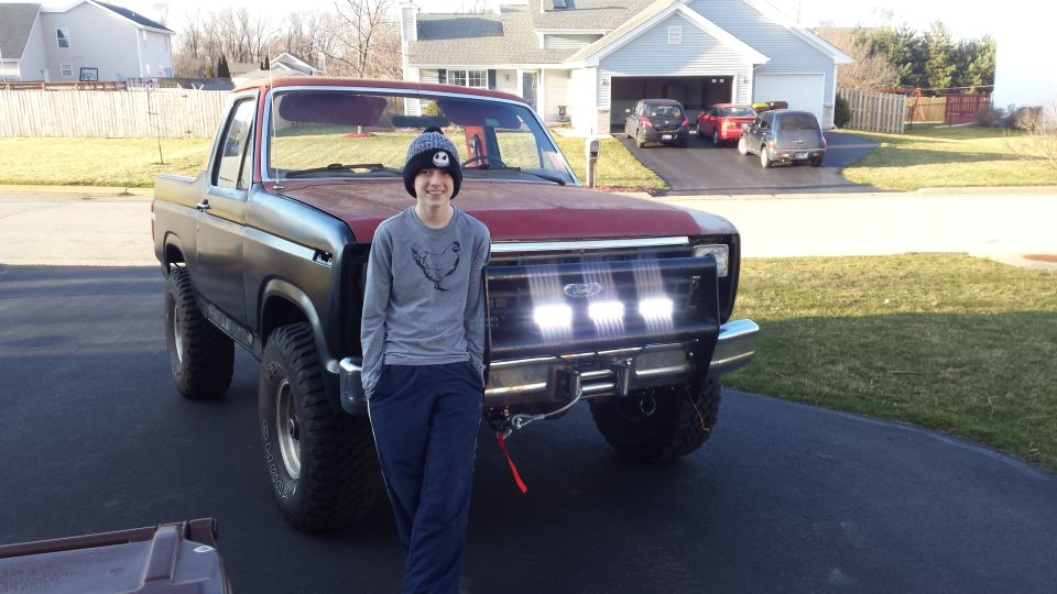 Person standing beside a lifted Ford Bronco with light bar in a driveway