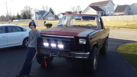 Person leaning on a lifted Ford Bronco with front light bar in a driveway