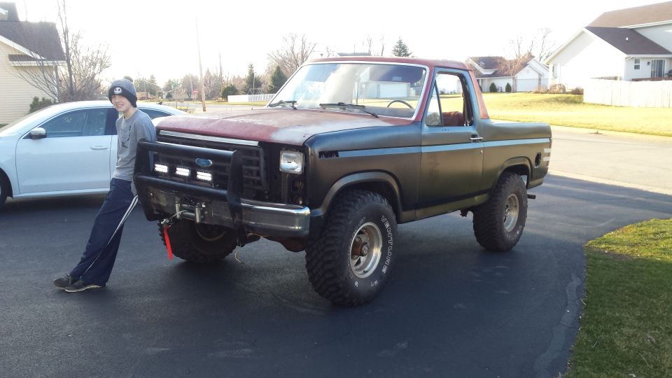 Person standing next to a lifted classic Ford Bronco in a driveway