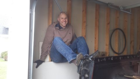 Man sitting and smiling on a panel inside a garage