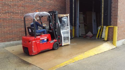 Red Raymond forklift carrying a wrapped pallet near a loading dock