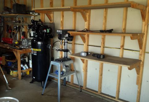 Air compressor and drill press against framed garage wall