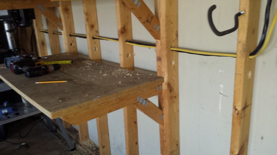 Plywood workbench shelf with electrical wiring along framed garage wall