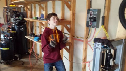 Person holding a tool in a garage workshop near an electrical panel