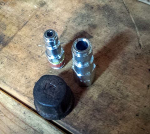 Two quick-connect air couplers and a cap on a wooden bench