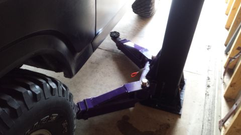 Purple two-post automotive lift arm positioned under a vehicle on a garage floor