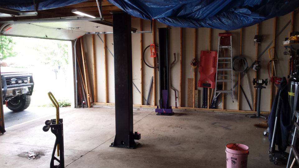 Garage interior with a black two-post lift column and tools on the wall
