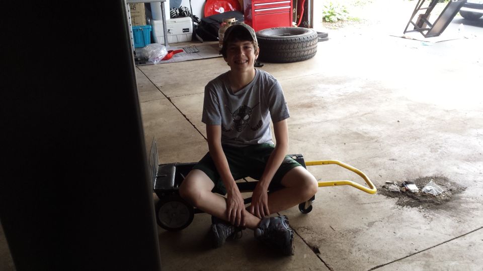 Young person sitting on a small cart on a garage floor