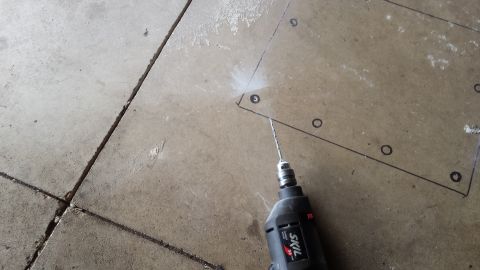 Drill boring an anchor hole inside a marked outline on a concrete floor