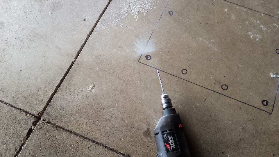 Drill boring an anchor hole inside a marked outline on a concrete floor