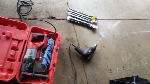 Rotary hammer drill, case, and bits laid on a concrete garage floor