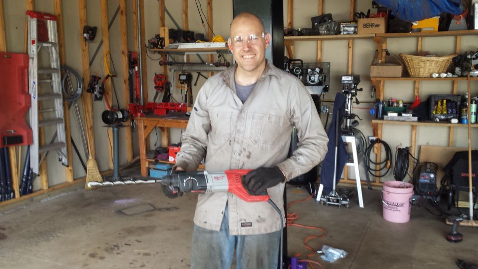 Man holding a rotary hammer drill in a tool-filled garage