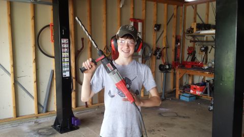 Young person holding a rotary hammer drill beside a two-post lift column