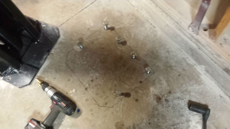 Concrete anchor bolts set in a marked square on a garage floor