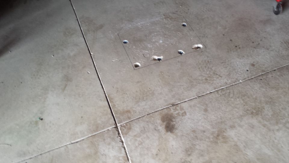 Patched square of concrete with anchor studs protruding from a garage floor