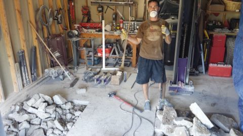 Man in dust mask standing amid broken concrete and tools in a garage