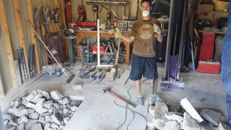 Man in dust mask standing amid broken concrete and tools in a garage