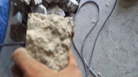Hand holding a chunk of broken concrete over a debris pile