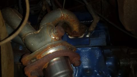 Rusty exhaust manifold and downpipe on a blue engine block