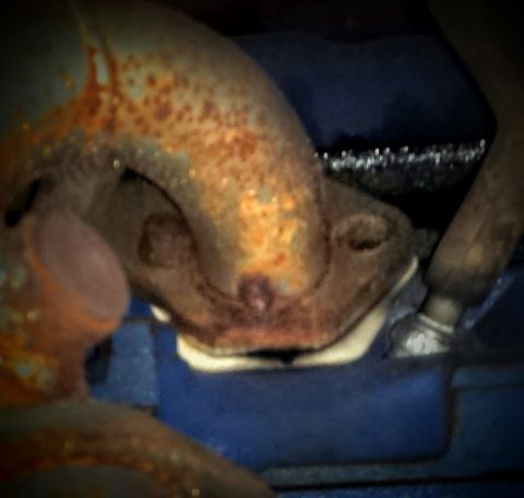 Extreme close-up of a corroded exhaust manifold on a blue engine