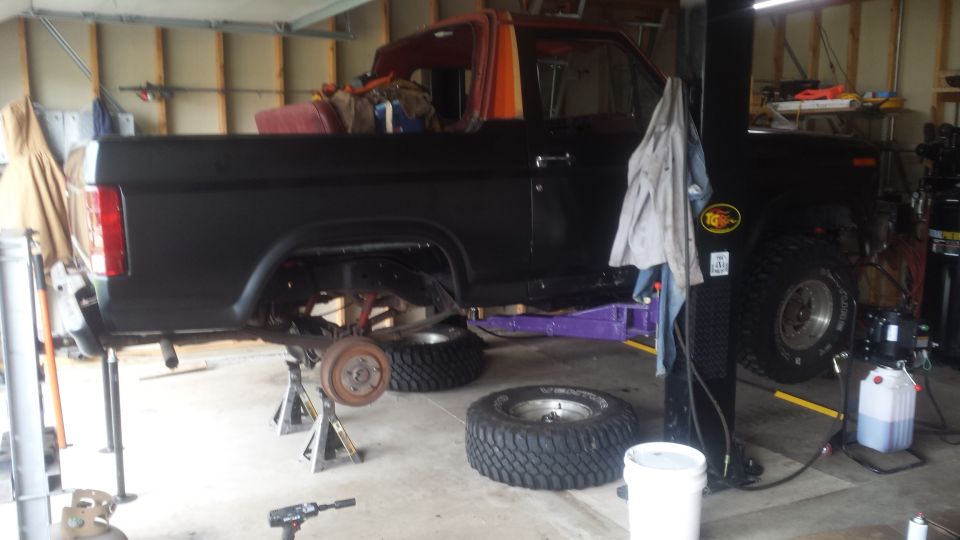 Black Ford pickup on jack stands with rear wheel removed inside a garage