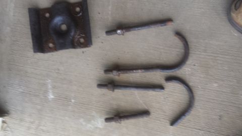 Spring shackle bracket, U-bolts, and threaded bolts laid on a wood surface